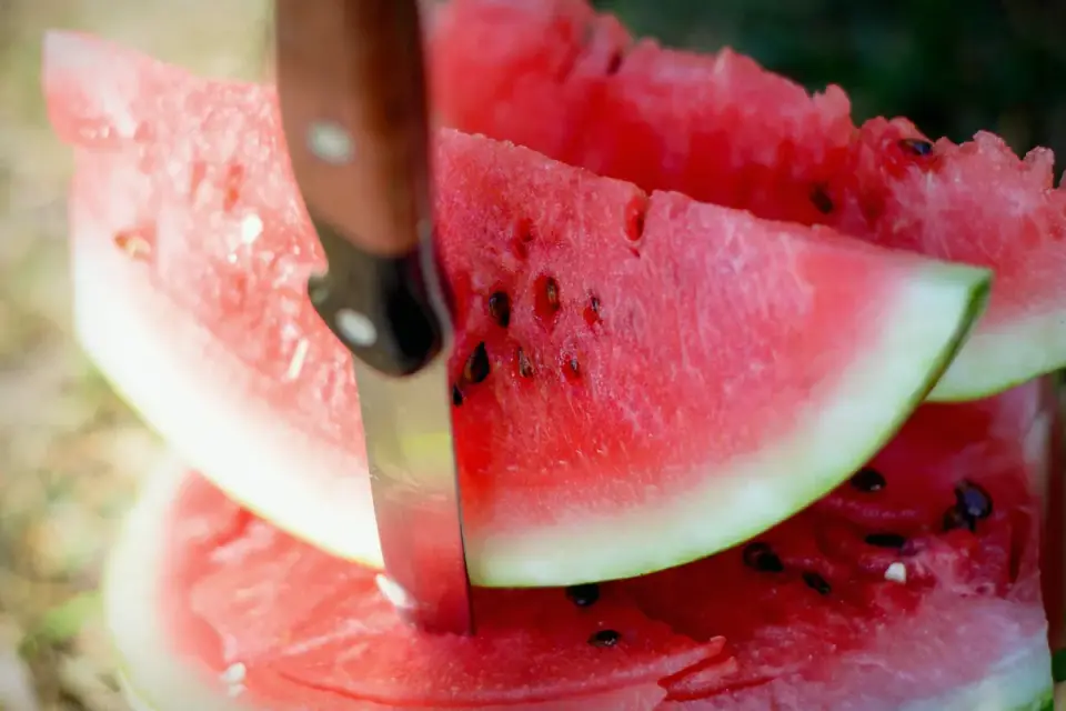 Watermelon rind being trimmed away from cubed fruit on a cutting board
